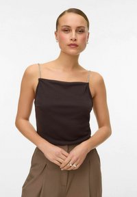 Zwarte mouwloze top met een vierkante halslijn, voorzien van dunne, glinsterende schouderbandjes. De stof lijkt glad en is gecombineerd met beige broeken.