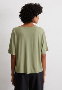 Olijfgroene, losse t-shirt gemaakt van zachte stof met korte mouwen en een wijde halslijn, met een rechte zoom en minimale stikdetails.