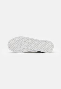 Semelle de sneaker blanche avec un motif géométrique texturé, présentant un bord cranté pour une meilleure adhérence et stabilité. Surface lisse avec des éléments de design minimalistes.