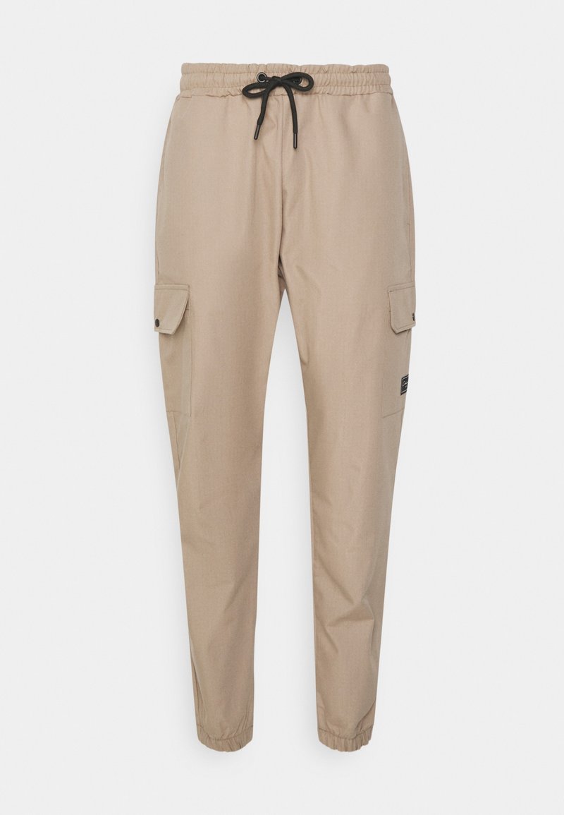 Pantalon cargo beige avec taille et poignets élastiques, cordon noir et poches à rabat de chaque côté.