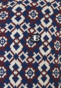 Neulekangas, jossa on geometrinen kuvio sinisessä, burgundissa ja kermassa, sekä mustavalkoinen "B"-logo. 