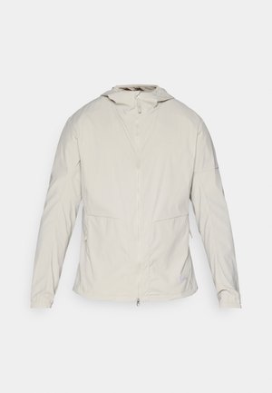 Light beige jacket, front zip closure, hood, elastic cuffs, two side pockets, and smooth, textured fabric. Minimalist design, no visible logos.