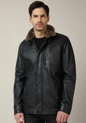 Czarna skórzana kurtka z kołnierzem z sztucznego futra, przednia kieszeń na zamek błyskawiczny oraz zapięcia na napy. Gładka tekstura z luźnym krojem.