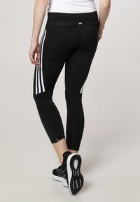 Černé sportovní legíny s bílými pruhy po stranách, přiléhavý design a zipy na kotnících pro přizpůsobení. Vyrobené z elastického materiálu.