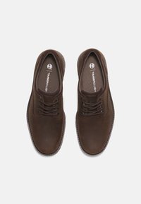 Scarpe in pelle marrone con una finitura liscia, dotate di punta rotonda, design con lacci e rivestimento in tessuto. Logo Timberland visibile all'interno.