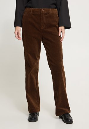 Pantalon droit en velours côtelé marron porté avec des chaussures noires et un haut noir à manches longues, montré de la taille aux pieds.