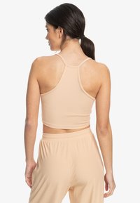 Light beige ribbed crop top with a scoop back and narrow straps, paired with matching ribbed high-waisted pants. Soft texture and elastic fit.