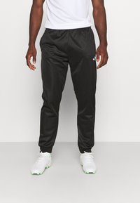 Zwarte sportbroek met een elastische tailleband en zijzakken, gemaakt van een gladde stof. Met een klein wit logo op de dij.