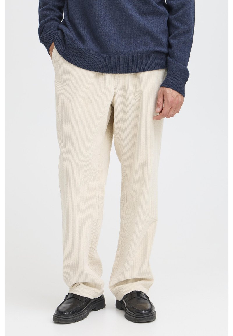 Beige corduroy pants with a ribbed texture, paired with a dark blue sweater, and black loafers. Minimalist design and relaxed fit.