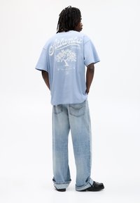 Light blue oversized t-shirt with white graphic design on back, text "Atlanta, Georgia," paired with light wash baggy jeans and black shoes.