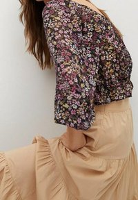 Kwiatowa bluzka z prześwitującego materiału, z rękawami o długości trzech ćwierć, w czarnym kolorze z kolorowymi wzorami. Połączona z miękką, beżową spódnicą w kant.