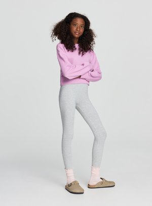 Leggings grigie abbinate a una felpa corta rosa. La modella indossa calzini rosa chiaro a coste e scarpe slip-on color talpa con suola piatta.