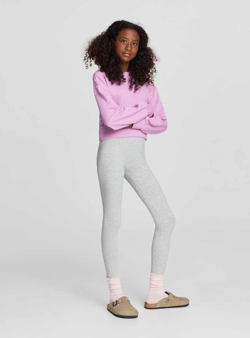 Leggings grigie abbinate a una felpa corta rosa. La modella indossa calzini rosa chiaro a coste e scarpe slip-on color talpa con suola piatta.