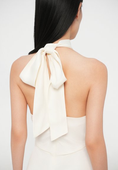Rochie albă cu guler halter și o fundă mare la spate. Material neted, ușor, cu un design cu spatele deschis și o strălucire subtilă.