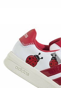 Baskets rouges et blanches avec des imprimés de coccinelles, dessus en cuir, semelle en caoutchouc, et trois bandes rouges. Comprend des accents texturés sur le talon.