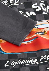 Dark gray sleeve over a black and gray checkered background with a red animated car face and white text reading Lightning McQueen.