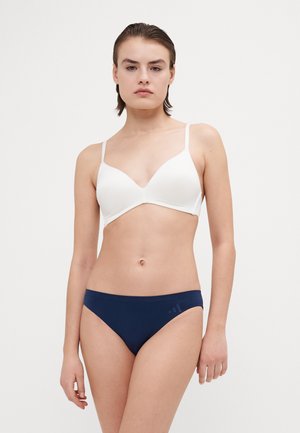Witte draadloze bh met een diepe V-hals en verstelbare schouderbanden, gecombineerd met marineblauwe low-rise bikini bottoms met een klein logo.
