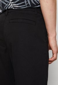 Svarta byxor med en slät textur, med en bakficka med passpoal. Designen inkluderar bälteslingor och sidogaft, med en slim fit.