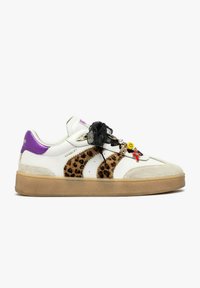 Sneaker bianca con strisce leopardate, linguetta sul tallone viola, suola beige, lacci neri decorati con charms tra cui una faccina sorridente e una croce rossa.