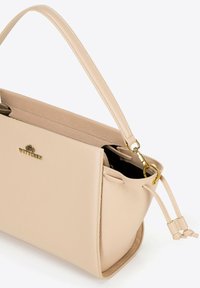 Beige leren handtas met een gestructureerd oppervlak en een enkele schouderband. Heeft een gouden logo, een open bovenkant en vastgebonden accenten aan de zijkanten.