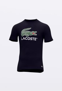 Tumesinine puuvillane lühikeste varrukatega T-särk, millel on roheline krokodillilogo ja valge "LACOSTE" tekst. Sile tekstuur, istuv disain.