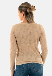 Maglione beige lavorato a maglia con un motivo a onda e una texture leggera. Maniche lunghe e collo a coste. Abbinato a jeans blu, con uno stile aderente.