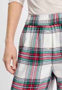 Gekleurde loungewear broeken hebben een gestructureerde stof met rode, groene en witte patronen, een elastische tailleband en decoratieve knoopdetails.