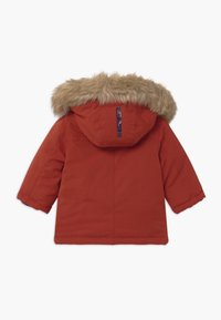 Parka rossa isolata con cappuccio rimovibile in pelliccia sintetica, caratterizzata da un esterno resistente e cuciture rinforzate per garantire calore.