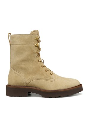 Tan suede nilkkurit, joissa on kultaiset metalliset rei'itysosat, nauhoitus edessä ja paksu ruskea kumipohja. Takana on vetoketju.