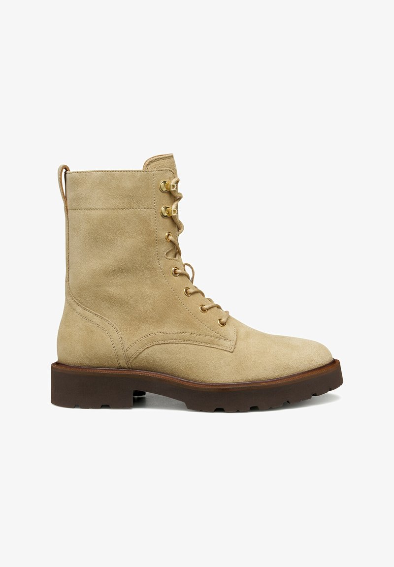 Stivaletto in suede tan con occhielli in metallo dorato, chiusura con lacci e suola in gomma marrone spessa. Presenta un manico sul retro.