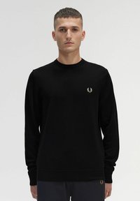 Schwarzer Langarmpullover aus weichem Stoff, mit Rundhalsausschnitt und einem kleinen goldenen gestickten Lorbeerlogo auf der linken Brust.