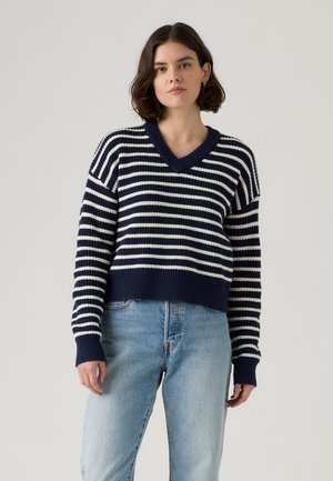 Marineblauw en witte gestreepte gebreide trui met een V-hals, cropped ontwerp en geribbelde manchetten, gecombineerd met lichtblauwe denim jeans.