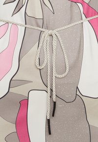 Fune bianche attorcigliate legate a fiocco su un tessuto con forme astratte nei toni di rosa, grigio, beige e bianco.