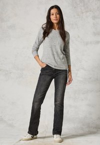 Grijze ribgebreide trui met lange mouwen, gecombineerd met zwarte denim jeans. Witte sneakers met minimale accenten maken de outfit af.