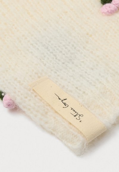 Πλεκτό κρεμ λευκό ύφασμα με μαλακή υφή, διακοσμημένο με ροζ ανθάκια και μπεζ ετικέτα με χειρόγραφτο κε�ίμενο.