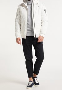Witte gewatteerde jas met capuchon, ritssluiting, zijzakken; grijze trui eronder, zwarte taps toelopende broek, marineblauwe sneakers met witte veters.