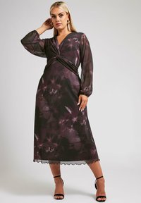 Długa, zwiewna sukienka z przezroczystej czarnej tkaniny z fioletowymi wzorami kwiatowymi. Posiada krój kopertowy, długie rękawy i falbaniasty dół.