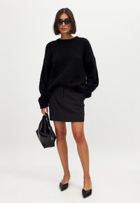 Maglione nero e fluffy con maniche oversize, abbinato a una gonna nera aderente. Gli accessori includono una borsa nera e occhiali da sole scuri.
