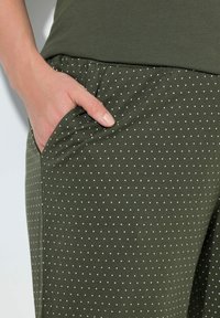 Pantalones livianos de color verde oliva con lunares blancos. Presentan una cintura elástica y un bolsillo lateral, mostrando una textura suave y un ajuste relajado.