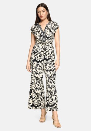 Sort og cremegul jumpsuit med blomsterprint, v-udskæring, kappelignende ærmer, taljebånd og vide ben, med et markant mønster og teksturerede detaljer.