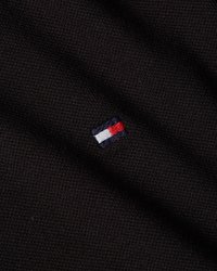 Tissu noir avec une surface texturée arborant un petit logo brodé en rouge, blanc et bleu. Aucun autre détail ou motif visible.