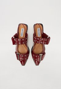 Chaussures slingback en cuir verni rouge avec bouts pointus, larges lanières avec œillets en argent et détails de boucle, semelles intérieures lisses couleur beige.