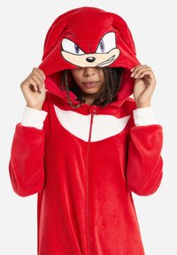 Red fleece onesie featuring a zip front and large hood with an embroidered character face. White accents decorate the chest and cuffs.