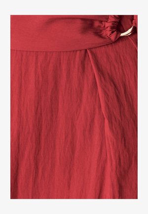 Tissu rouge texturé avec une taille froncée et un design drapé. Surface lisse avec des rides subtiles, mettant en valeur la structure du vêtement.