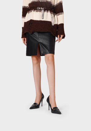 Donna con gonna in pelle nera con spacco frontale, maglione a righe marrone e crema con cintura e scarpe nere a punta con tacco alto.