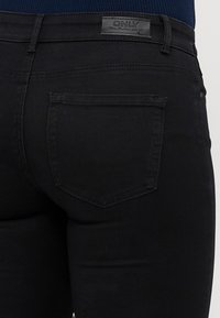 Melnas džinsas ar gludu tekstūru, ar aizmugures kabatu un izšuvumu. Jostasvieta ir ar zīmola etiķeti "ONLY."