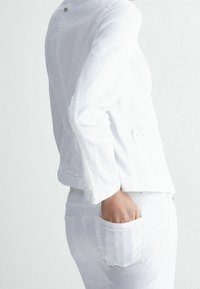 Bílá džínsová bunda s límcem, vpředu na knoflíky a bočními kapsami, spárovaná s bílými džíny s zadními kapsami a přiléhavým střihem.