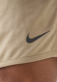 Pantalones cortos deportivos de malla color beige con un logo en forma de swoosh negro de Nike. Presenta costuras visibles a lo largo del dobladillo, enfatizando la textura y el material.