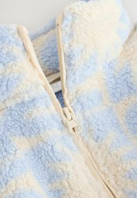 Close-up of a soft fleece fabric in light blue and cream with a white zipper partially zipped.