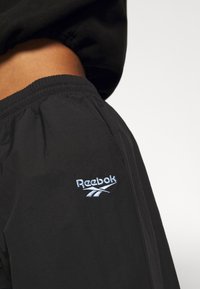Los pantalones cortos negros de Reebok cuentan con una cinturilla elástica y un logo bordado en azul en la pierna izquierda, fabricados con material ligero.